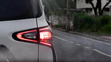 Driving of white car on the asphalt road. Signal of brake light. Side road with green grass and tree. and blurred of house. Front view has a blurry mist. photo