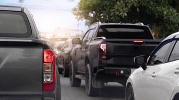 Rear side of pickup car gray color with turn on brake light. Many car stop at a traffic light at an intersection. With tree side of road. Bright light shines from the front and there is a city. photo