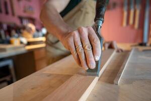 Closeup professional carpenter hand using chisel to smooth wood board surface removing imperfections photo