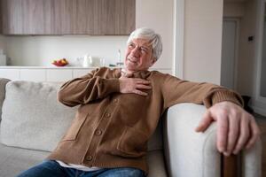 Distressed old man in pain suffers on sofa clutching chest, myocardial infarction heart attack photo