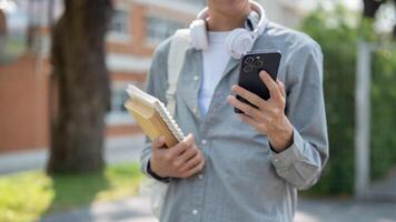 Close up of man looking at smartphone in left hand and books in right hand standing on street. photo