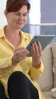 In cozy home setting, middle-aged woman lounges on couch, indulging in junk food as she thoughtfully explores digital content on tablet. Perfect fusion of relaxation, technology, and casual style video