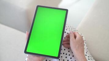 Top view of hands gripping tablet showcasing bright green screen, engaging with interactive visuals in inviting indoor space. Digital mockup emphasizes chroma key tech for effortless screen swaps video
