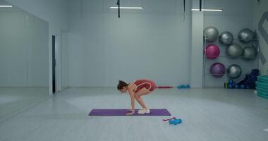 Girl athlete performs a burpee exercise in a modern gym setting during daytime fitness training session video