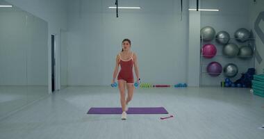 Girl athlete demonstrates reverse lunges with dumbbells in a modern gym setting video