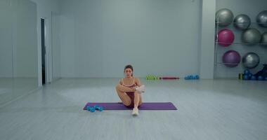 Girl athlete performs seated piriformis stretch in a fitness studio during a workout session focused on flexibility and recovery video