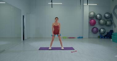 Girl athlete performs wide stance RDL exercise with dumbbells in gym training session video