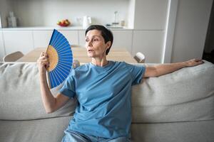 Exhausted mature woman fanning herself at home. Unbearable heat, elderly suffering from stuffy photo