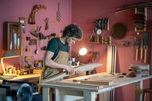 Serious dedicated carpenter working with wooden furniture part on workshop bench preparing shipment photo