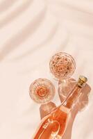 Glasses of rose wine on pink background with palm leaf shadows from sunlight. Minimal Top view Vintage wineglasses and bottle, sparkling alcohol drink above view, caustics from hard light, copyspace photo