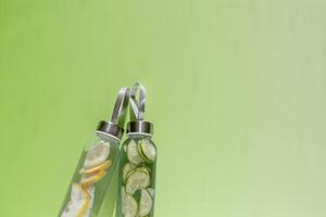 Glass bottles with lemon, cucumber water drink detox at sunlight on green colored background, copy space. Healthy infused water boost metabolism, weight loss. Aesthetic still life, refreshing drinks photo