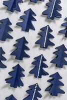 Minimal pattern from Blue Christmas trees cut out of paper on white fur, winter holiday vertical background. Homemade origami blue tree firs decorated pearl beads. Aesthetic top view, xmas holidays photo