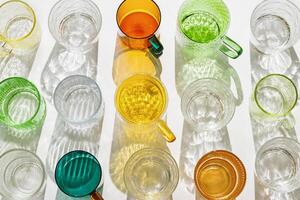 Set colored glass cups from transparent and clear glasses with beautiful shadow at sunlight, summer drink for events or relaxation, minimal aesthetic top view, creative summer drink backdround photo