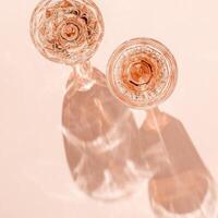 Wine Glasses of rose wine on light pink background, sun flare and reflection from sunlight. Aesthetic layout from various crystal glasses, sparkling alcohol drinks, champagne, Summer romantic setting photo