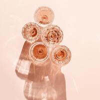 Minimal summer party concept, set glasses of rose wine or champagne on pink with shadows and light reflections. Bright shine wineglass with sparkling alcohol drink at sunlight, top view monochrome photo