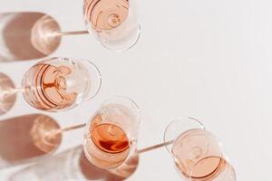 Set of glasses of rose wine at wine tasting, Minimal trend concept. Top view crystal wineglass standing at sunlight, shadow and sun glare, beige pink colored, alcohol drink background, copyspace photo
