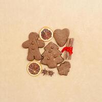 Christmas gingerbread cookies, biscuits, dry oranges sliced, cinnamon sticks on beige baking paper. Top view brown trend pattern, flat lay holiday sweet food, traditional bakery, new year photo