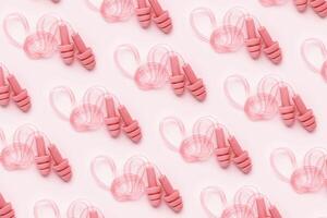 Creative pattern made powder pink silicone earplugs for swim, sleep, rest on pink background. Comfort ear plug on string against noise, protect hear, top view flat lay, visual trend concept photo