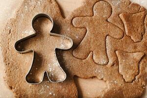 Cooking ginger cookies, Christmas and New Year traditional cookies in shape of gingerbread man, raw rolled out dough with cut out dough figures, closeup texture, top view, metal pastry cutter on dough photo