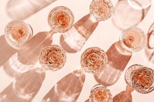 Minimal pattern of Top view glasses of rose wine or champagne on soft pink background, artistic shadows and sun glare. Aesthetic still life crystal wineglass, sparkling drinks for summer party photo