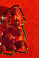 Plate as New Year tree with shining red Christmas balls on red textile, Christmas tree from green glowing glass glare. Sunlight and shadow, sparkling holiday food, xmas trendy still life photo