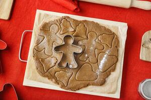 Preparation Cooking ginger cookies on red linen tablecloth background, Christmas and New Year holiday cookies in varios shapes, cutting biscuits with metal cookie cutters, wooden rolling pin photo