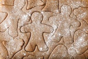 Cooking ginger cookies, Christmas and New Year traditional cookies in shape of gingerbread man, raw rolled out dough with cut out dough figures, closeup texture, top view, pattern on dough, above photo