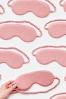 Minimal pattern from pink textile sleep masks on white light background. Woman hand take eye mask, comfort rest and quality sleep concept. Creative aesthetic top view composition photo