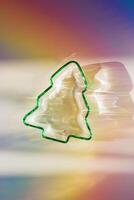 Green colored glass form as New Year tree, Christmas fir at sunlight with beautiful shadows and sparkling sun glare on rainbow gradient background. Winter holiday concept, minimal aesthetic photo