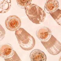Minimal summer party concept, glasses of rose wine or champagne on pink with shadows and light reflections. Bright shine wineglass with sparkling alcohol drink at sunlight, top view monochrome pattern photo