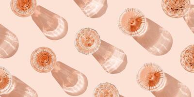 Minimal summer party banner, glasses of rose wine or champagne on pink with shadows and light reflections. Bright shine wineglass with sparkling alcohol drink at sunlight, top view monochrome photo