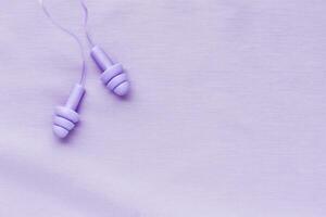 Reusable silicone earplugs purple color on colored cloth background, copy space. Soft, flexible ear plug on cord, for swim, sleep, against noise, protect hear, monochrome top view, minimal style photo