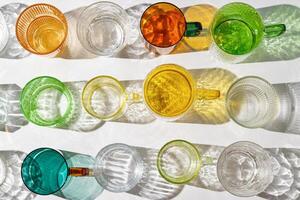 colored glass cups from transparent and clear glasses with beautiful shadow at sunlight, summer drink for events or relaxation, minimal aesthetic top view, creative summer drink backdround photo