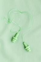 Reusable silicone earplugs green color on colored cloth background, copy space. Soft, flexible ear plug on cord, for swim, sleep, against noise, protect hear, monochrome top view, minimal trend photo