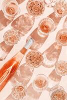 above glasses and bottle of rose wine on peach color background with beautiful shadows at sunlight. Vintage wineglass minimal style pattern, closeup sparkling alcohol drink, summer drink concept photo