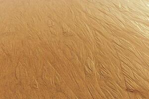 Sunlit Golden Sand with Rippled Texture from sea waves, wet shiny sandy shore at sunset, yellow beige natural textured pattern, minimal nature surface, summer time photo