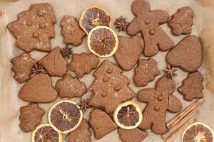 Christmas gingerbread cookies, biscuits, dry oranges sliced, cinnamon sticks on beige baking paper. Top view brown trend pattern, flat lay holiday sweet food, traditional bakery, photo