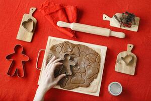 Top view preparing Cooking ginger cookies, Christmas and New Year traditional cookie in shape of gingerbread man, raw rolled out dough, woman hands holding metal pastry cutter on dough photo