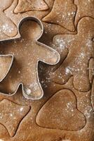 Cooking ginger cookies, Christmas and New Year traditional cookies in shape of gingerbread man, raw rolled out dough with cut out dough figures, closeup texture, top view, metal pastry cutter photo