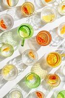 Vivid Glasses with cold detox water as summer still life pattern, shadow and sunlight refraction, closeup glass cups of infused fruit water, slises of lemon, orange, healthy summer drinks photo