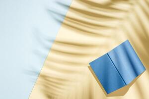Summer minimal background with shadow of palm tree leaf and book on light yellow and blue paper. photo
