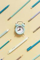 Creative Flat lay with clock and geometric pattern from blue pens and pencils on beige Time to go to school concept photo