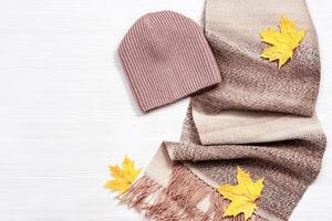 Autumn comfortable clothes and decorative yellow maple leaves. Scarf and cap for woman photo