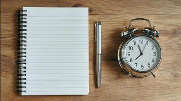 Notepad pen and alarm clock on wooden table ready for business work or studying time management photo