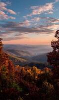 Autumnal panoramic vista showcases rolling mountains framed by colorful trees under a vibrant skyscape at sunset photo