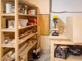 Organized woodworking shop featuring tools, drill press, materials, and shelving packed with supplies, set in a clean and functional creative workspace photo