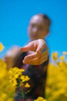 Close-up of girl reaching towards camera with silver jewelry on her arm, holding handcrafted round straw bag in blooming rapeseed field. photo