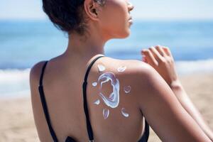 A woman joyfully applies sunscreen at the beach, savoring the ocean view on a sunny day photo