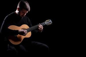 A man is playing an acoustic guitar on a black background photo