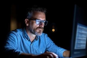 A man in glasses is working on a computer at night photo